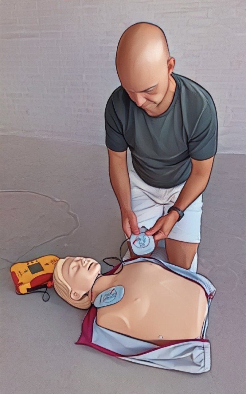 Deltager placerer defibrillator-elektroder på øvelsesdukke